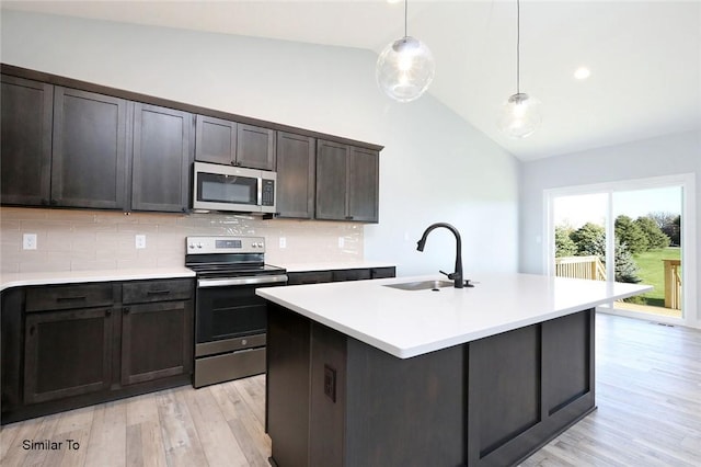 kitchen featuring light wood finished floors, light countertops, lofted ceiling, appliances with stainless steel finishes, and a sink