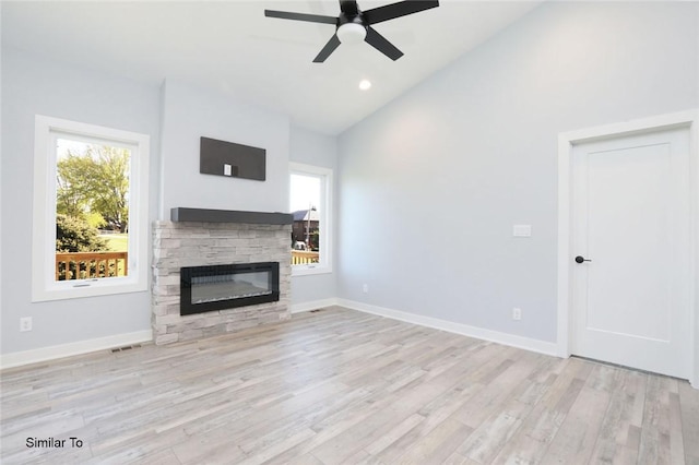 unfurnished living room with light wood finished floors, ceiling fan, baseboards, vaulted ceiling, and a stone fireplace