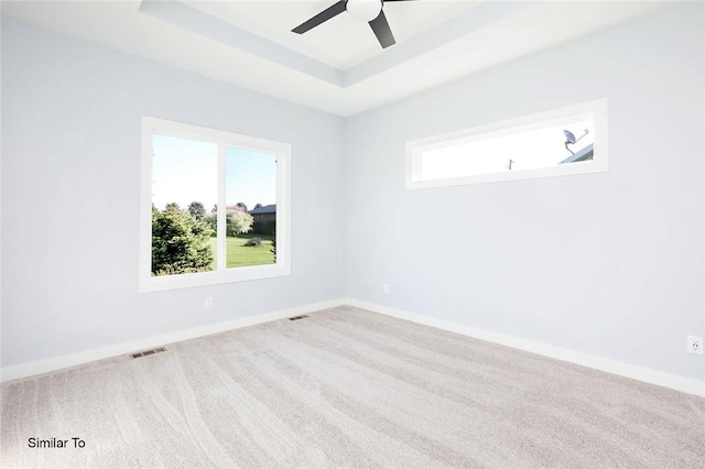 carpeted empty room with visible vents, a ceiling fan, a raised ceiling, and baseboards