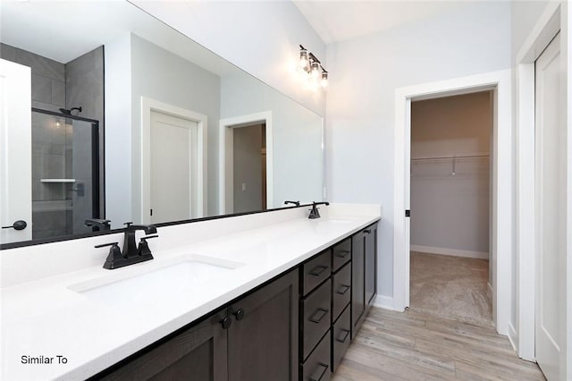 bathroom with wood finished floors, tiled shower, double vanity, a sink, and a walk in closet