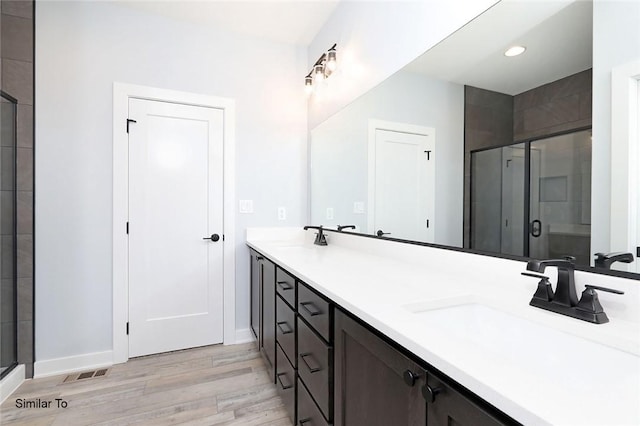 bathroom featuring double vanity, a stall shower, wood finished floors, and a sink