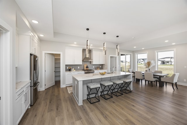 kitchen featuring white cabinets, wall chimney range hood, dark hardwood / wood-style floors, an island with sink, and decorative light fixtures