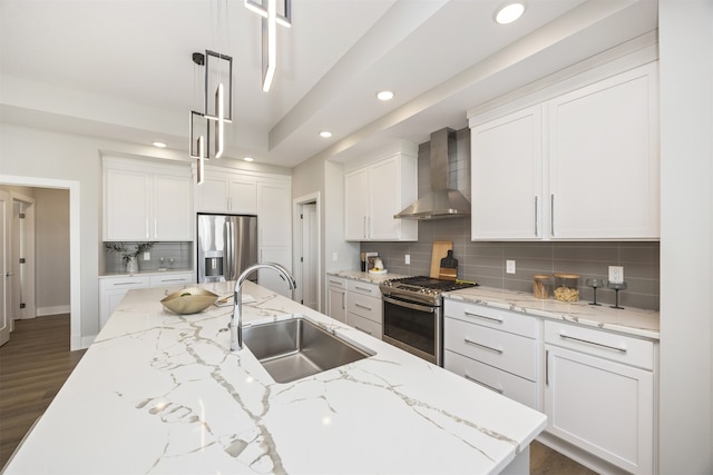 kitchen with stainless steel appliances, sink, wall chimney range hood, white cabinets, and hanging light fixtures