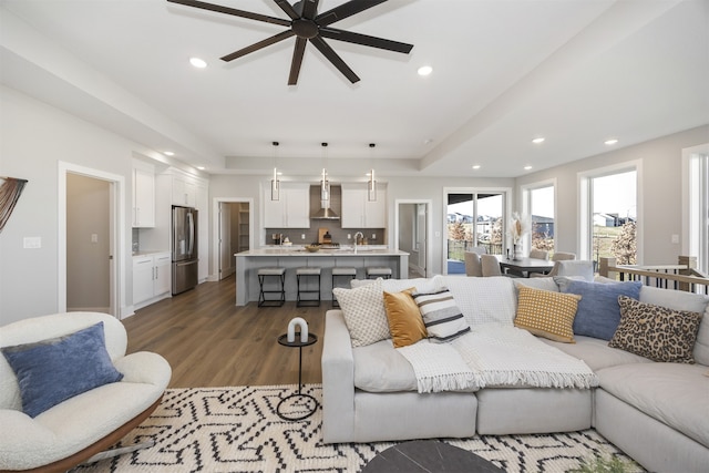 living room featuring dark hardwood / wood-style floors, ceiling fan, sink, and a tray ceiling