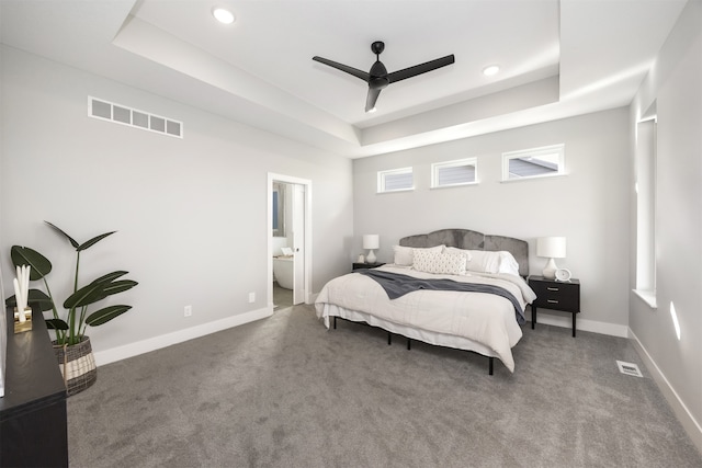 bedroom featuring a raised ceiling, connected bathroom, ceiling fan, and carpet