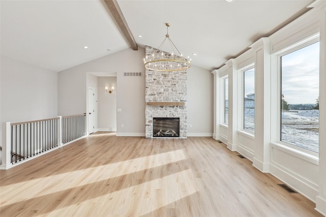 unfurnished living room featuring lofted ceiling with beams, a stone fireplace, a wealth of natural light, and an inviting chandelier