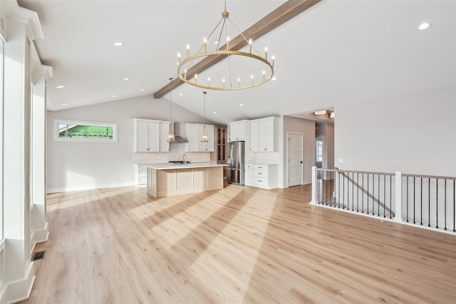 kitchen featuring pendant lighting, stainless steel fridge, an island with sink, tasteful backsplash, and beam ceiling