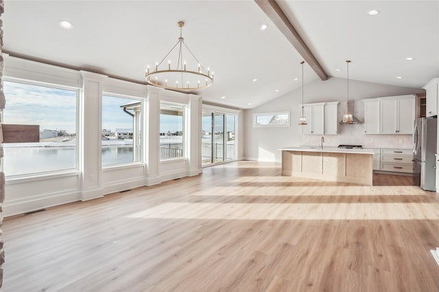 kitchen featuring stainless steel refrigerator, white cabinetry, wall chimney exhaust hood, an island with sink, and decorative light fixtures