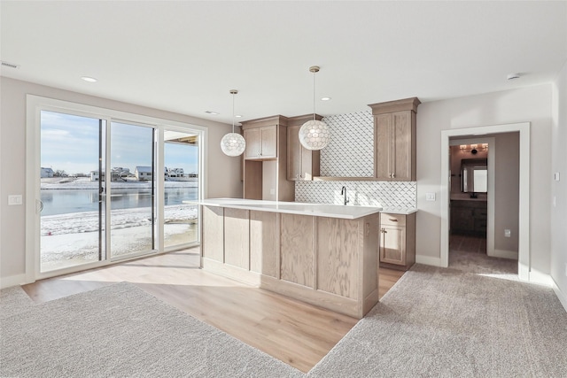 kitchen with decorative backsplash, light colored carpet, pendant lighting, a water view, and a center island