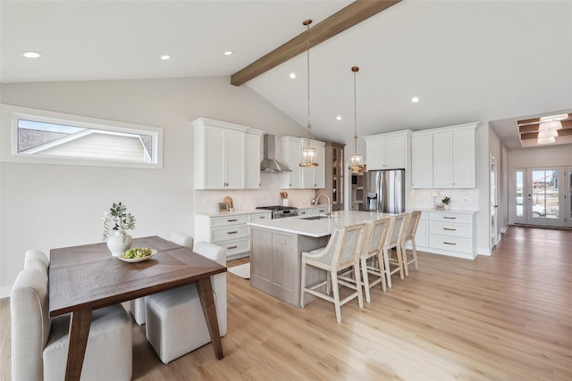 kitchen featuring white cabinets, hanging light fixtures, light countertops, appliances with stainless steel finishes, and wall chimney exhaust hood