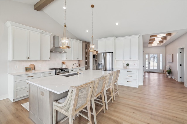 kitchen with a kitchen island with sink, a sink, light countertops, appliances with stainless steel finishes, and wall chimney exhaust hood