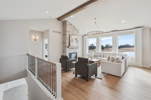 living area with lofted ceiling with beams, a stone fireplace, a notable chandelier, visible vents, and light wood-type flooring