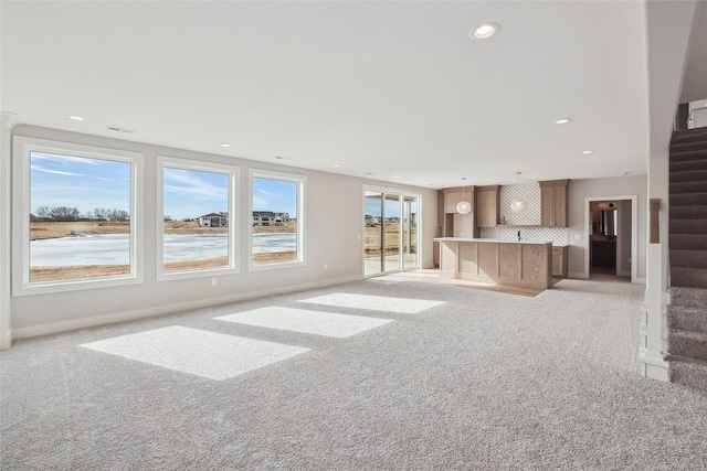 unfurnished living room with stairs, a water view, light carpet, and recessed lighting