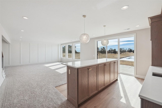 kitchen featuring a decorative wall, open floor plan, light countertops, hanging light fixtures, and a center island