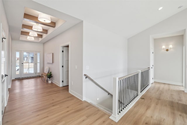 hall featuring lofted ceiling with beams, baseboards, light wood-style flooring, and an upstairs landing