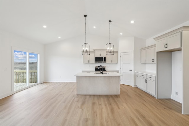 kitchen with lofted ceiling, a center island with sink, sink, hanging light fixtures, and light hardwood / wood-style floors