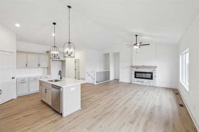 kitchen with decorative light fixtures, a center island with sink, dishwasher, a stone fireplace, and lofted ceiling