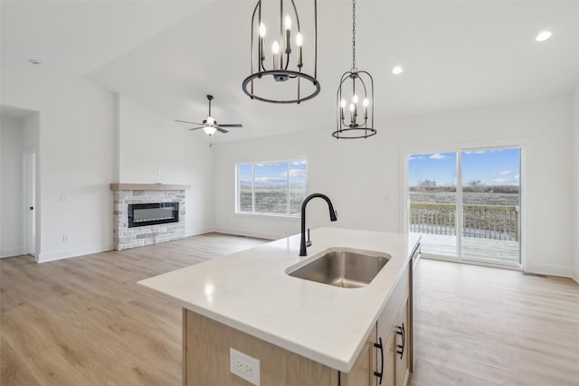 kitchen featuring pendant lighting, a center island with sink, a stone fireplace, sink, and light hardwood / wood-style flooring