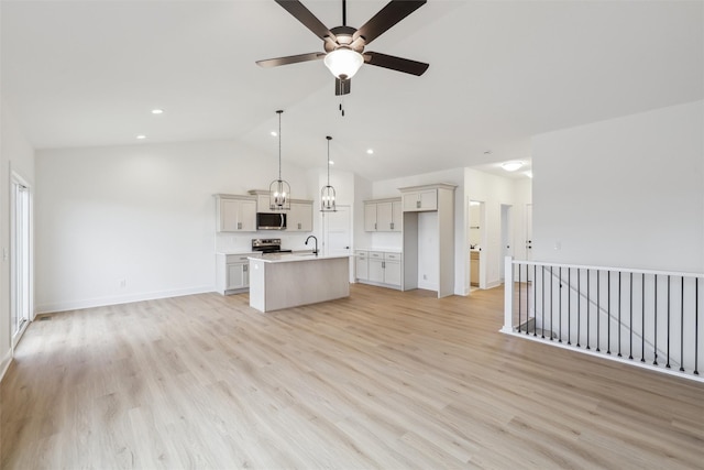 kitchen with hanging light fixtures, lofted ceiling, a kitchen island with sink, appliances with stainless steel finishes, and light wood-type flooring