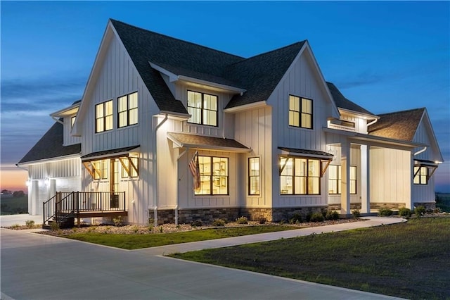 back of property at dusk featuring board and batten siding, a yard, and a shingled roof