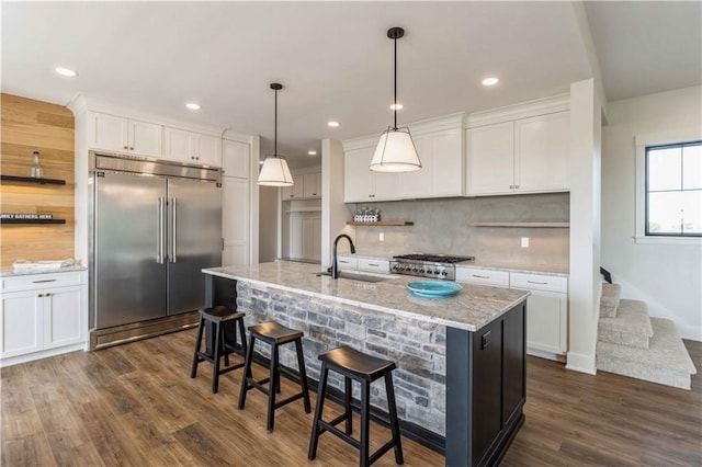 kitchen featuring an island with sink, appliances with stainless steel finishes, white cabinetry, dark wood-type flooring, and sink