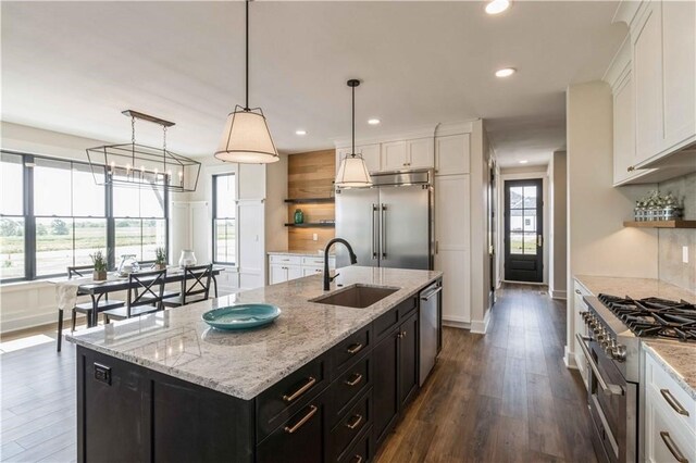 kitchen with an island with sink, sink, decorative light fixtures, premium appliances, and white cabinetry