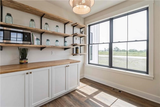 interior space featuring dark wood-style flooring, stainless steel microwave, visible vents, and baseboards