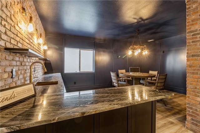 kitchen featuring sink, hardwood / wood-style floors, dark brown cabinetry, an inviting chandelier, and stone counters