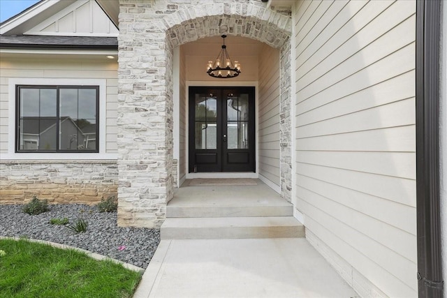 view of exterior entry with stone siding, a shingled roof, board and batten siding, and french doors