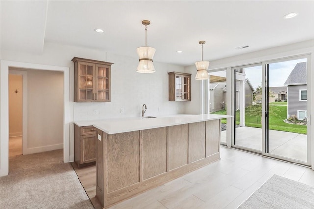 kitchen featuring pendant lighting, light countertops, visible vents, glass insert cabinets, and a kitchen island