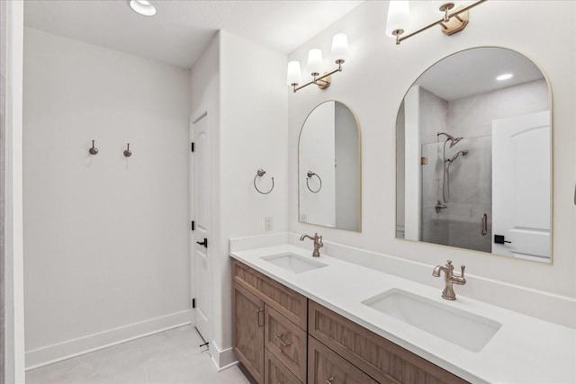 bathroom featuring double vanity, walk in shower, a sink, and baseboards