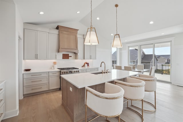 kitchen with lofted ceiling, a sink, light wood-style floors, light countertops, and an island with sink