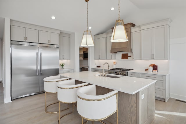 kitchen with light wood finished floors, vaulted ceiling, stainless steel appliances, light countertops, and a sink