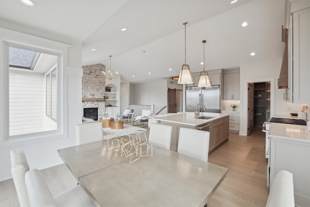 kitchen with lofted ceiling, light wood-style flooring, a sink, high end appliances, and a center island with sink