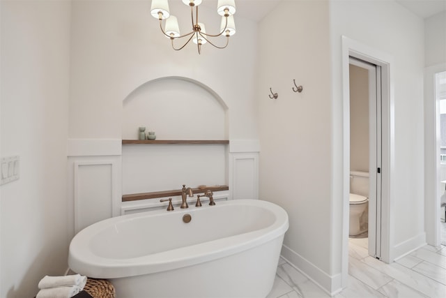 bathroom with marble finish floor, a notable chandelier, a soaking tub, toilet, and baseboards