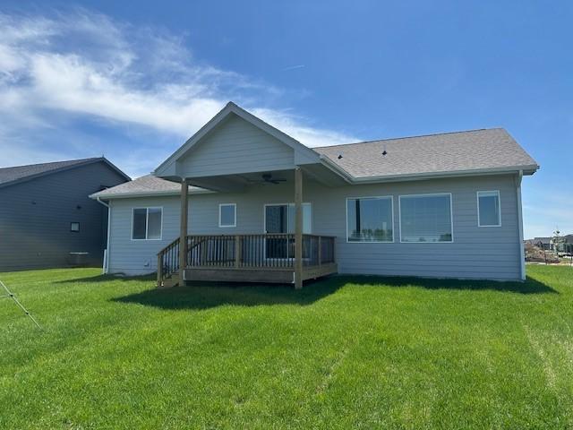 back of property featuring a deck, a ceiling fan, and a lawn