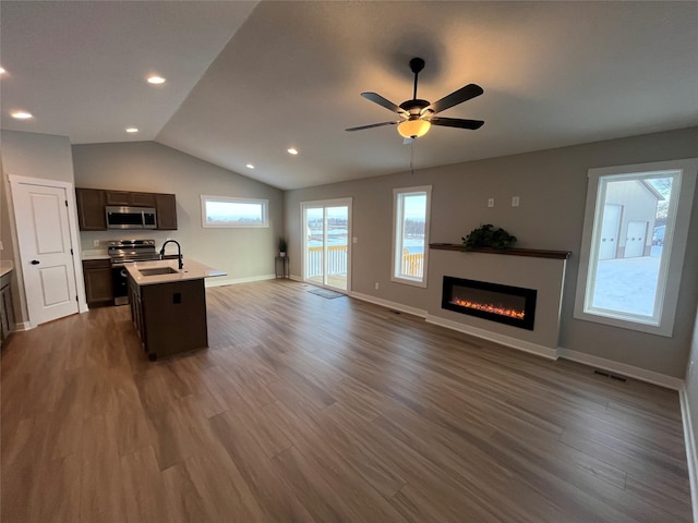 kitchen featuring dark brown cabinets, stainless steel appliances, a kitchen island with sink, dark wood-type flooring, and lofted ceiling