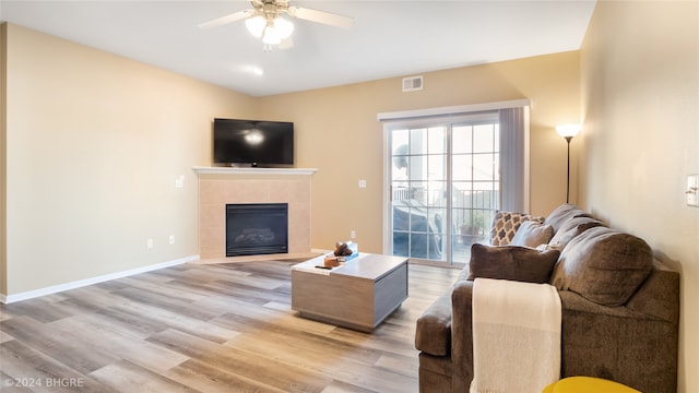 living room featuring light hardwood / wood-style flooring, a tile fireplace, and ceiling fan