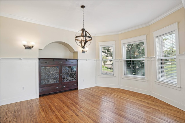 empty room with hardwood / wood-style floors, crown molding, a wealth of natural light, and a chandelier