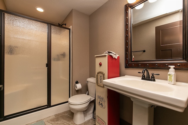 bathroom featuring a shower with shower door, toilet, and sink