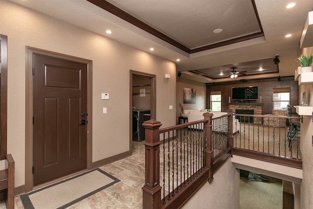 entryway featuring a textured ceiling, a fireplace, a tray ceiling, ornamental molding, and ceiling fan