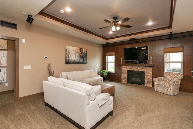 living room with a raised ceiling, ceiling fan, a stone fireplace, and carpet