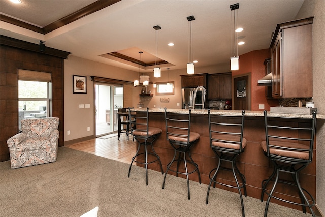 kitchen with a kitchen bar, stainless steel refrigerator with ice dispenser, kitchen peninsula, hanging light fixtures, and a tray ceiling