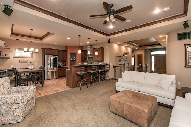 living room with ceiling fan with notable chandelier, light hardwood / wood-style floors, a raised ceiling, and crown molding