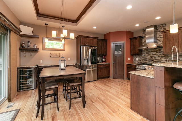 kitchen with decorative light fixtures, stainless steel appliances, wall chimney range hood, wine cooler, and dark brown cabinetry