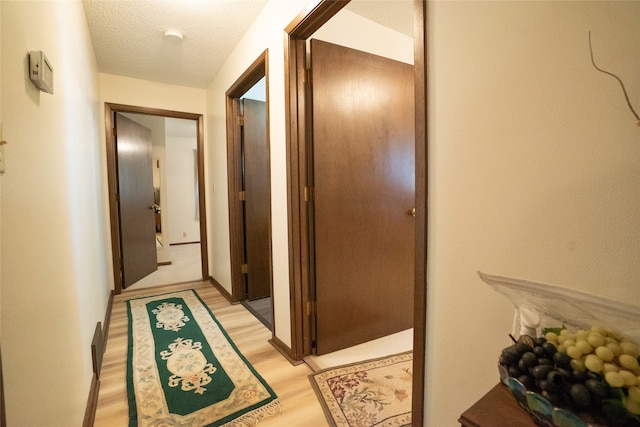 corridor with a textured ceiling and light hardwood / wood-style floors