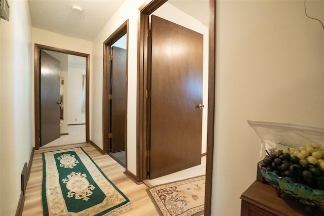 hall with a textured ceiling and light hardwood / wood-style flooring