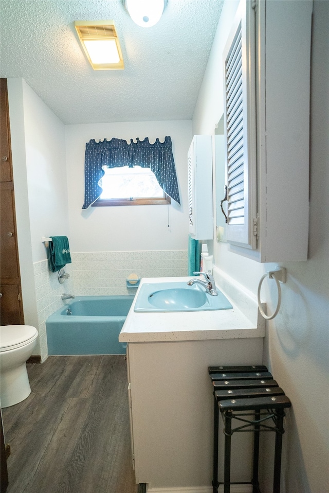 bathroom featuring hardwood / wood-style floors, toilet, a tub, vanity, and a textured ceiling