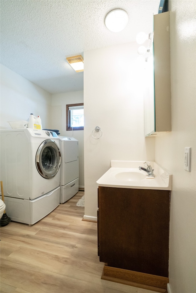 laundry area with washing machine and clothes dryer, sink, a textured ceiling, and light hardwood / wood-style floors