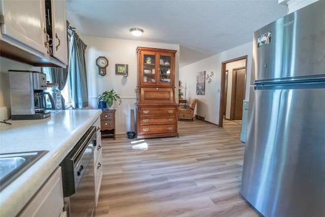 kitchen with appliances with stainless steel finishes, a textured ceiling, and light hardwood / wood-style flooring